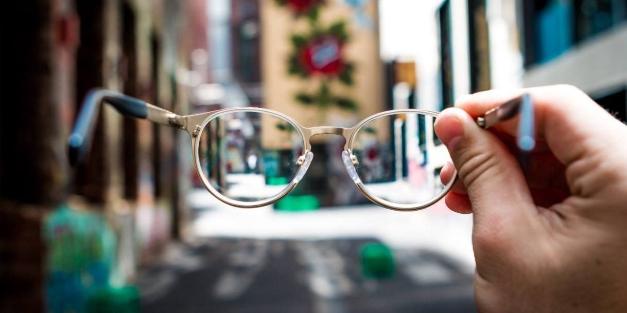 a person holds up a pair of glasses in front of a street that is out of focus